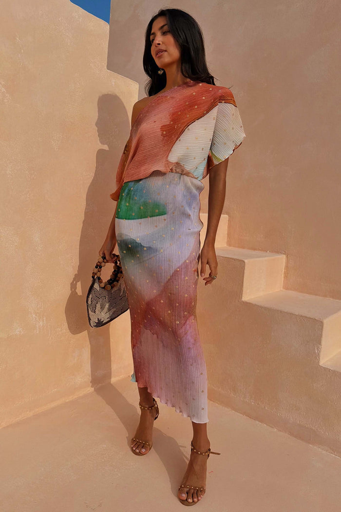 Abstract Tilly midaxi dress with metallic gold flecks and a multi-coloured print on a model standing against stone stairs.
