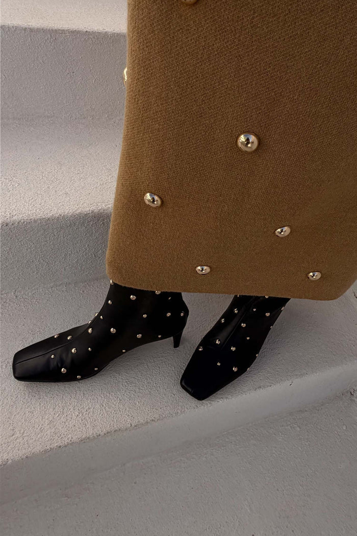 Black Leather Boots with gold studs and a square toe, styled with a textured camel skirt on white steps.