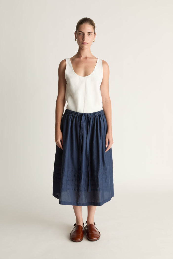 Woman wearing a white top and navy skirt on a plain background