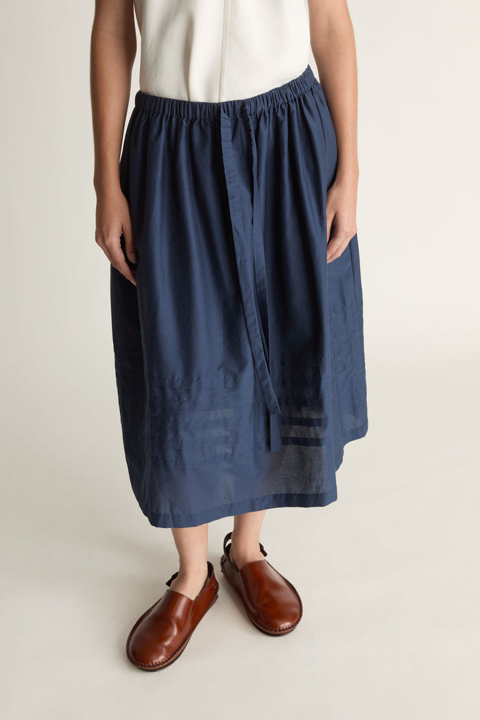 Woman wearing a white top and navy skirt on a plain background