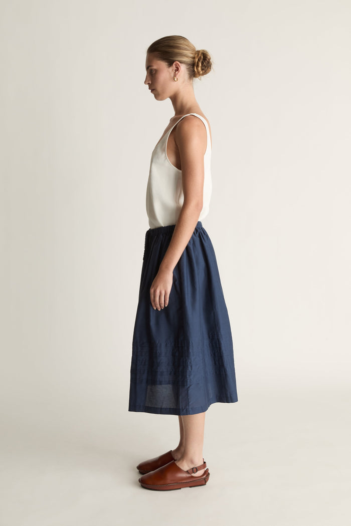 Woman wearing a white top and navy skirt on a plain background