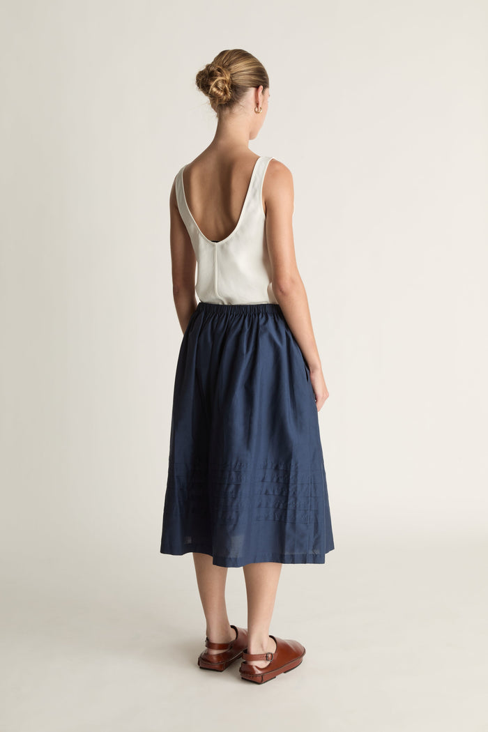 Woman wearing a white top and navy skirt on a plain background