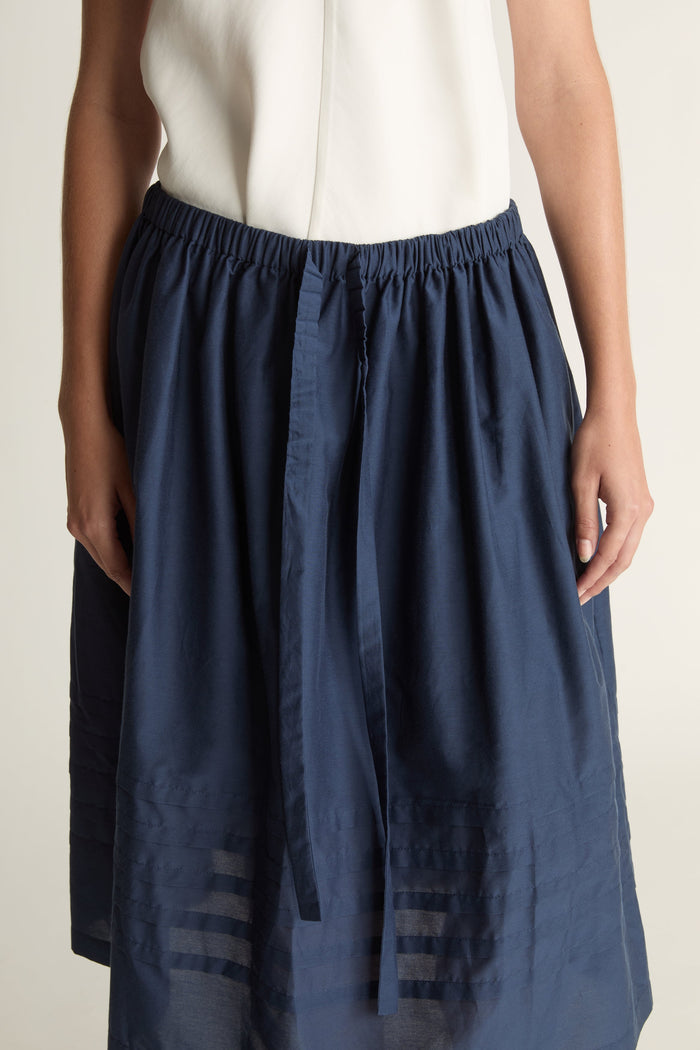Woman wearing a white top and navy skirt on a plain background
