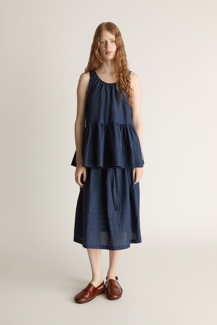 Woman wearing navy blue blouse with a gathered detail and a navy blue skirt on a white background