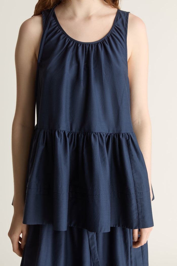 Woman wearing navy blue blouse with a gathered detail and a navy blue skirt on a white background