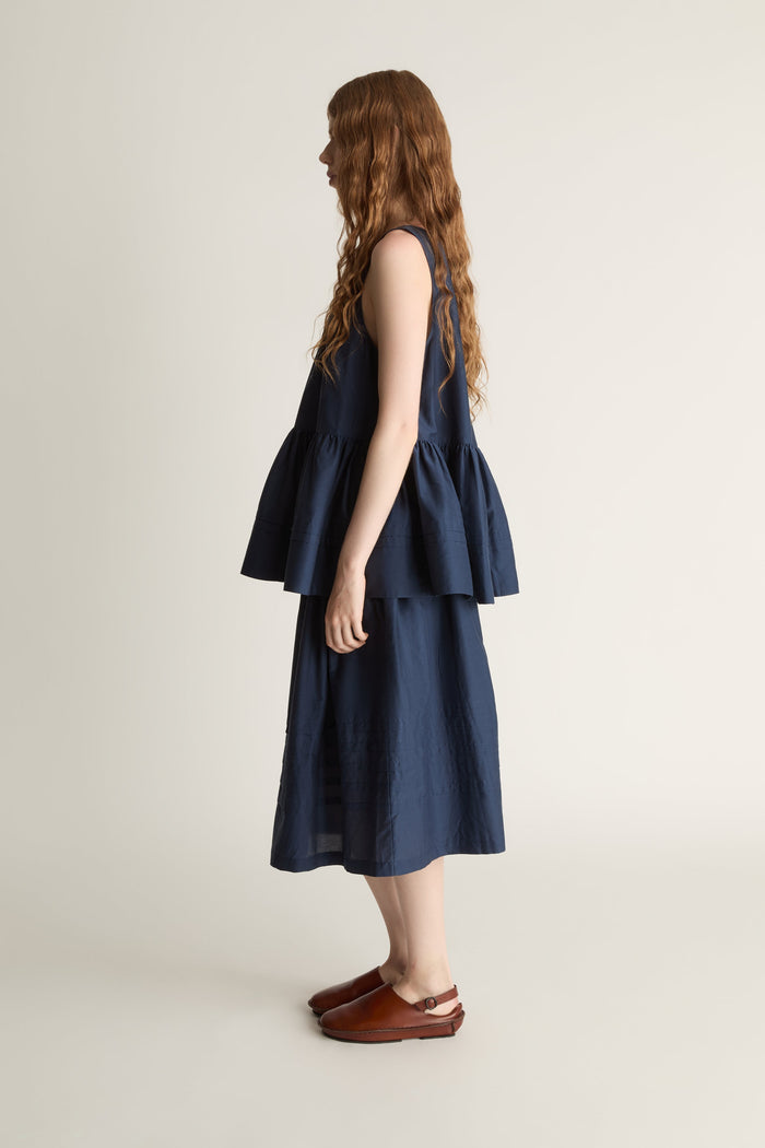 Woman wearing navy blue blouse with a gathered detail and a navy blue skirt on a white background