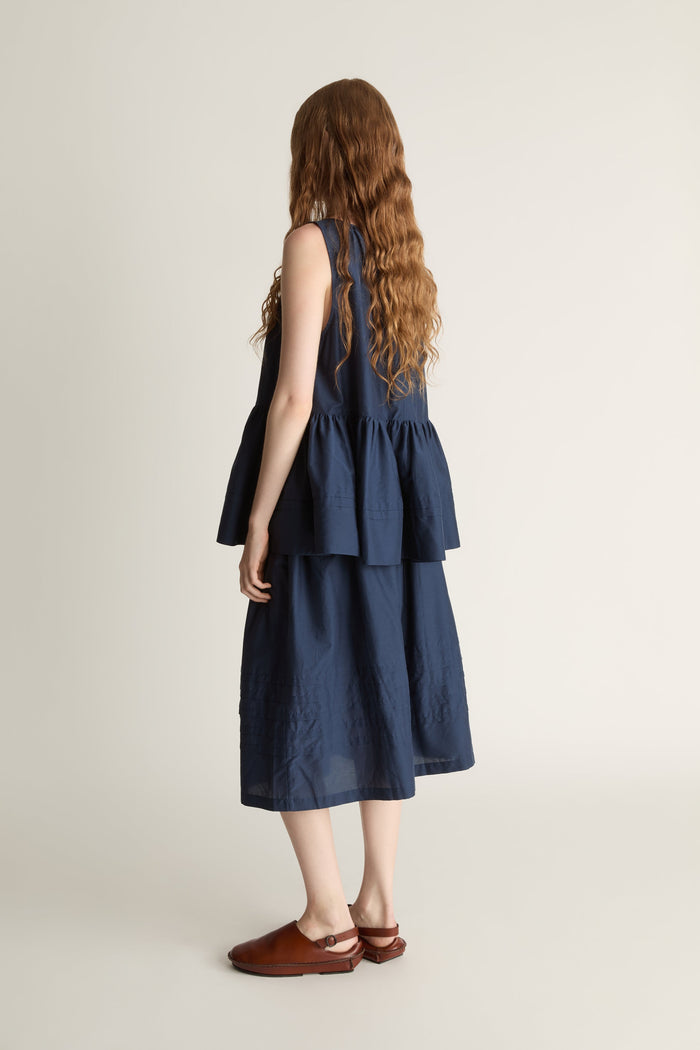 Woman wearing navy blue blouse with a gathered detail and a navy blue skirt on a white background
