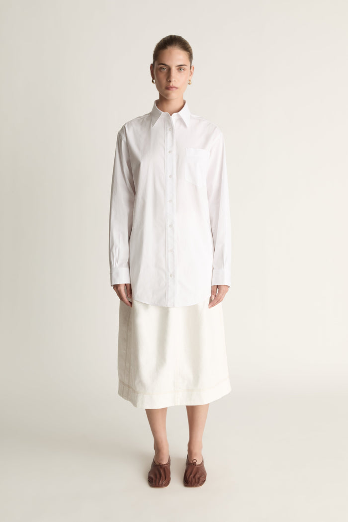 Person wearing a long white shirt and skirt on a plain background