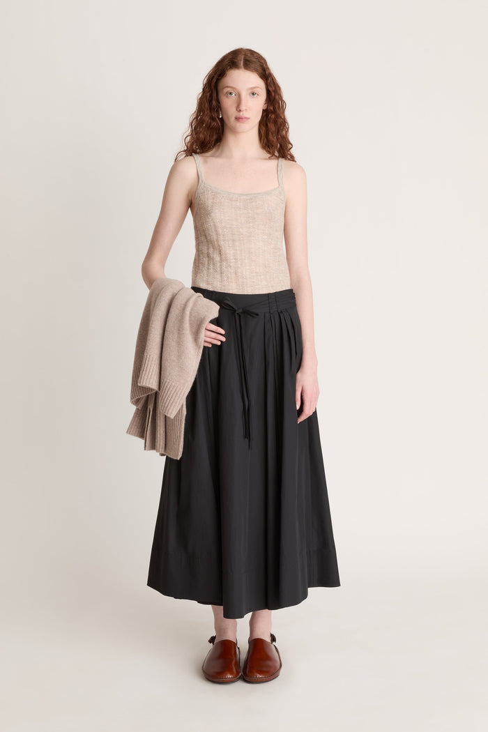 Woman wearing a beige top and black skirt with a beige cardigan on a white background