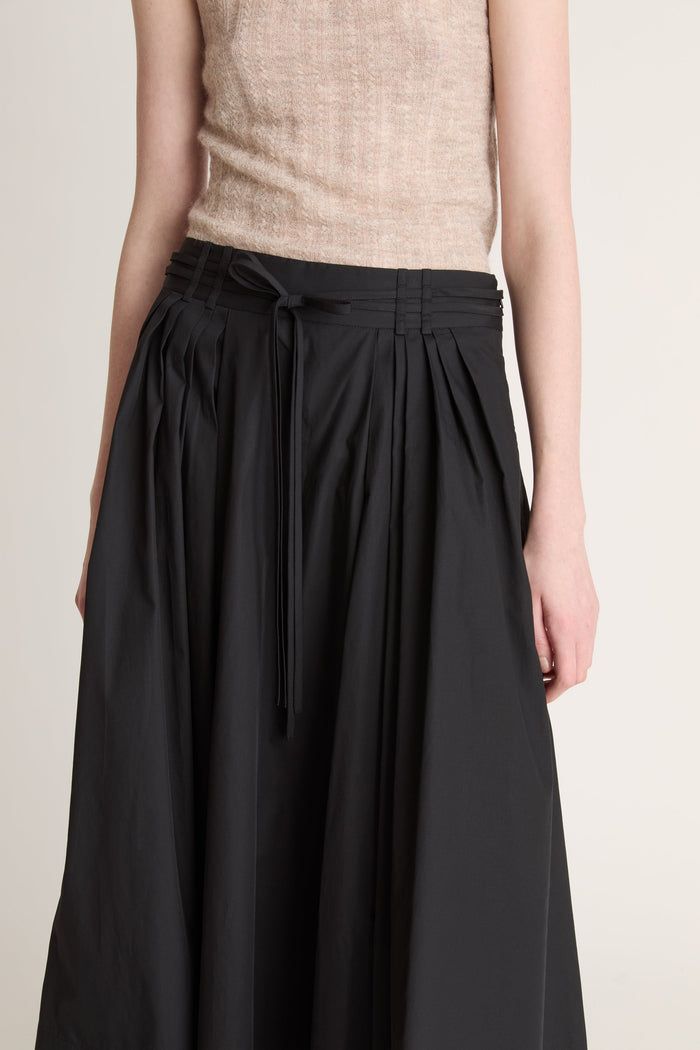 Woman wearing a beige top and black skirt with a beige cardigan on a white background