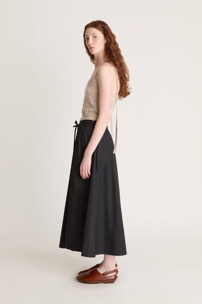 Woman wearing a beige top and black skirt with a beige cardigan on a white background