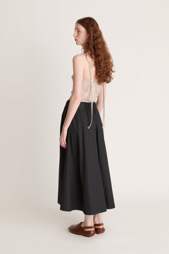 Woman wearing a beige top and black skirt with a beige cardigan on a white background