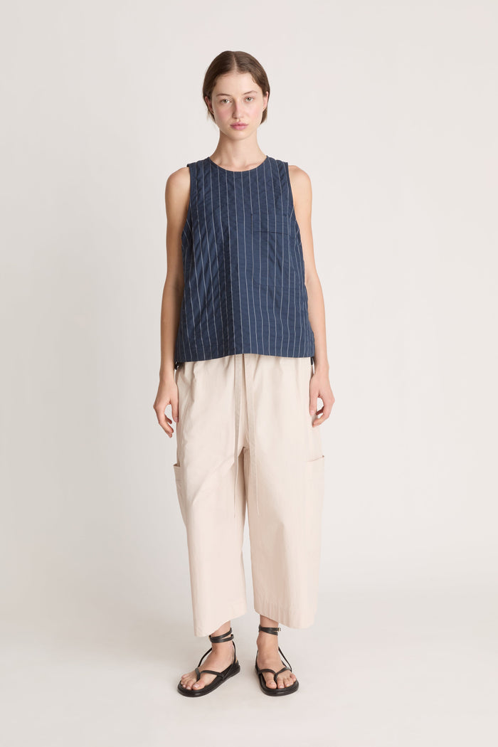 Woman wearing a sleeveless striped top and beige pants on a white background