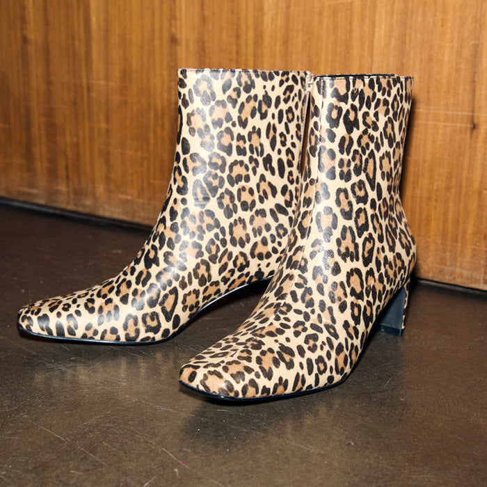 Leopard Heel Boots with a square toe and thin block heel, featuring a leopard print pattern against a wooden backdrop.