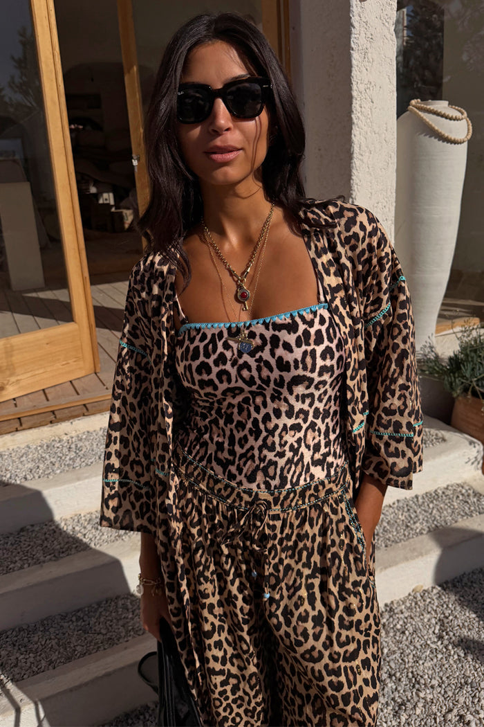 Leopard print bandeau swimsuit with blue whipstitch trim, matching balloon trousers and shirt in a vacation setting.