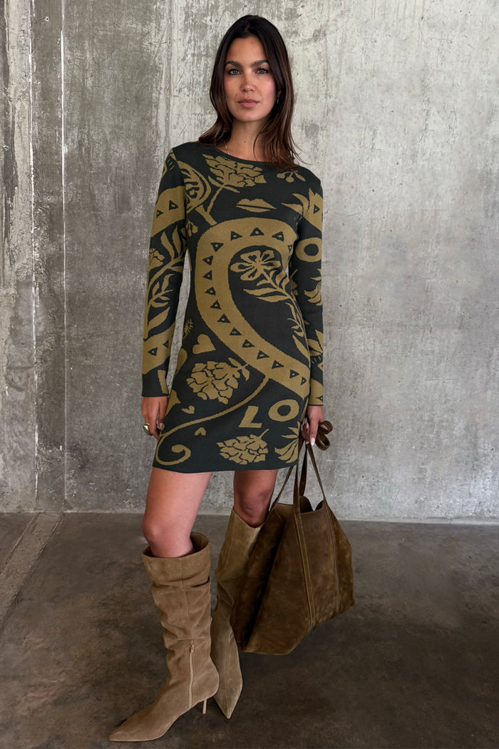 Olive Amara Knit Mini Dress with iconic motifs, styled with tall tan boots and a large brown suede tote bag.