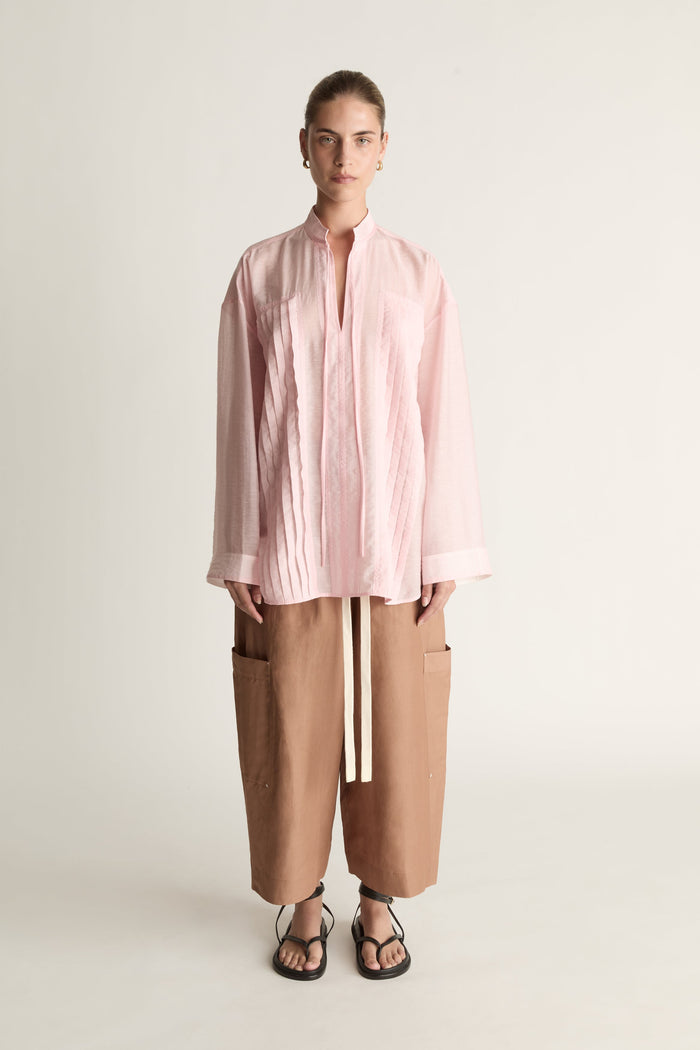 Person wearing a light pink shirt and brown pants on a white background