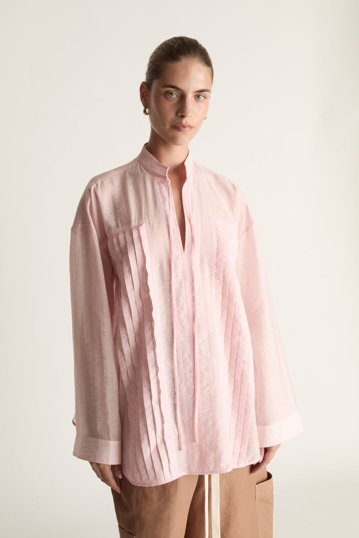 Person wearing a light pink shirt and brown pants on a white background