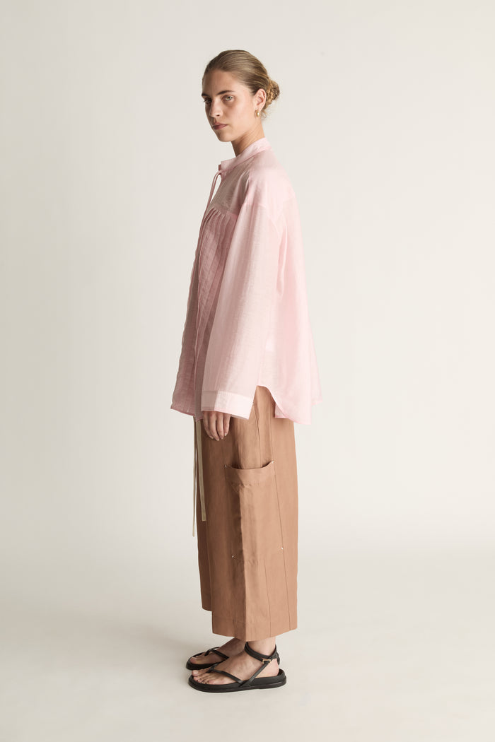 Person wearing a light pink shirt and brown pants on a white background