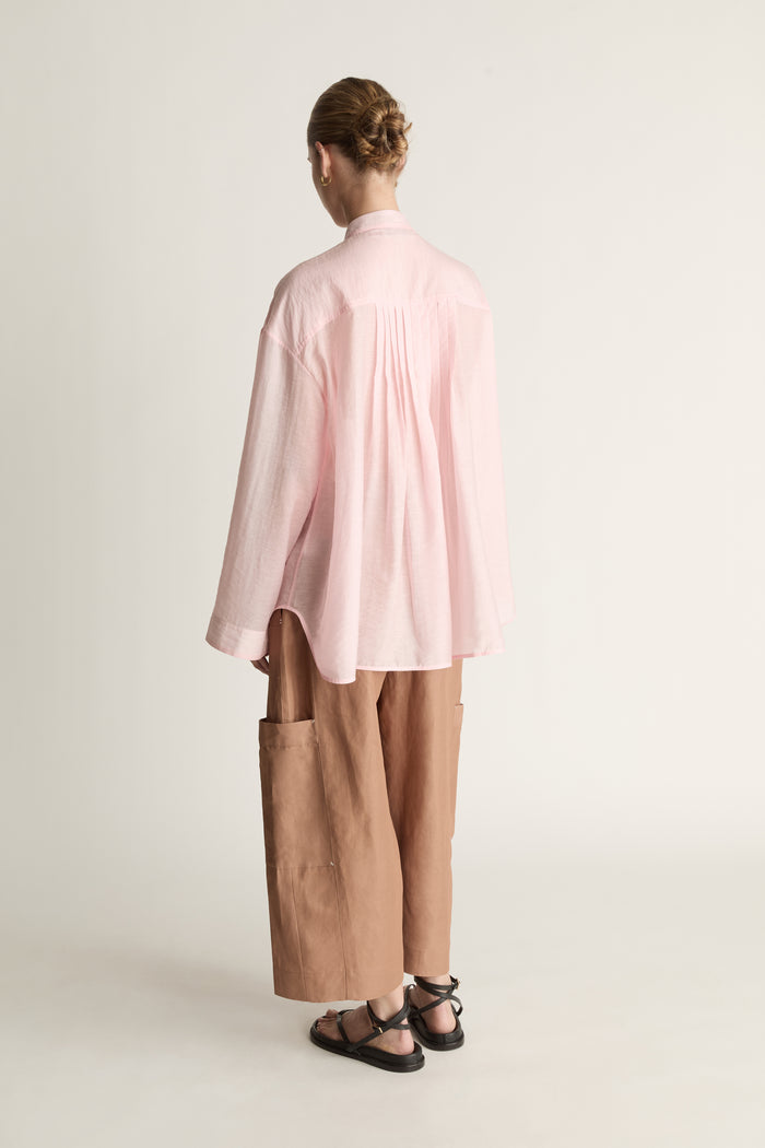 Person wearing a light pink shirt and brown pants on a white background
