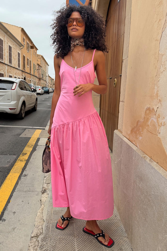Pink Strappy Nova Dress featuring a dropped waist and full midaxi skirt, styled on a city street for a vacation look.