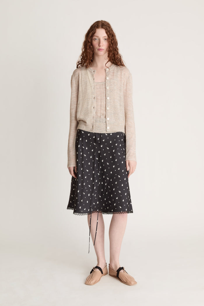Woman wearing a beige knit cami top and cardigan with a black printed skirt on a white background