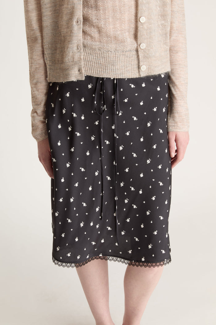 Woman wearing a beige knit cami top and cardigan with a black printed skirt on a white background