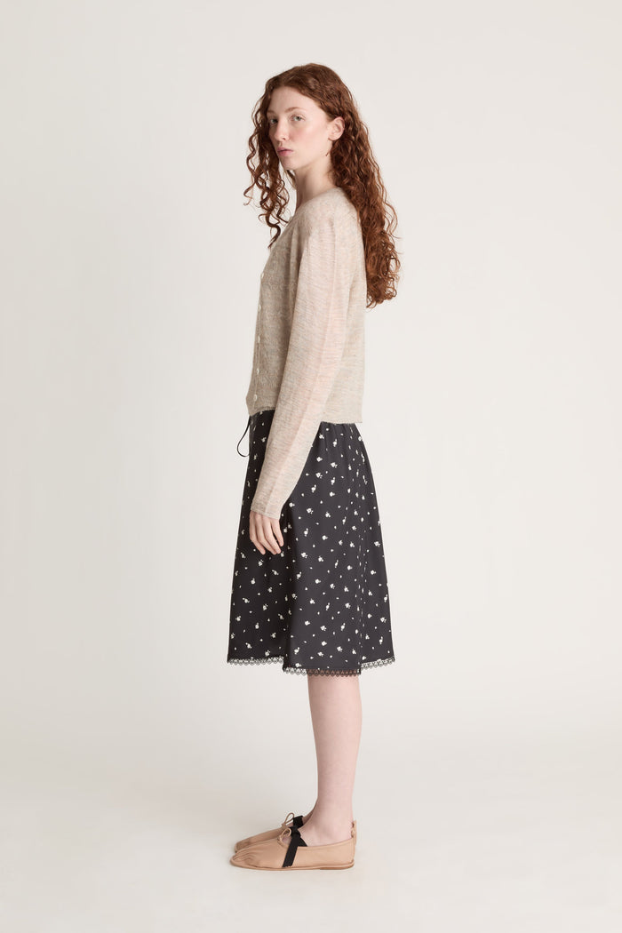Woman wearing a beige knit cami top and cardigan with a black printed skirt on a white background