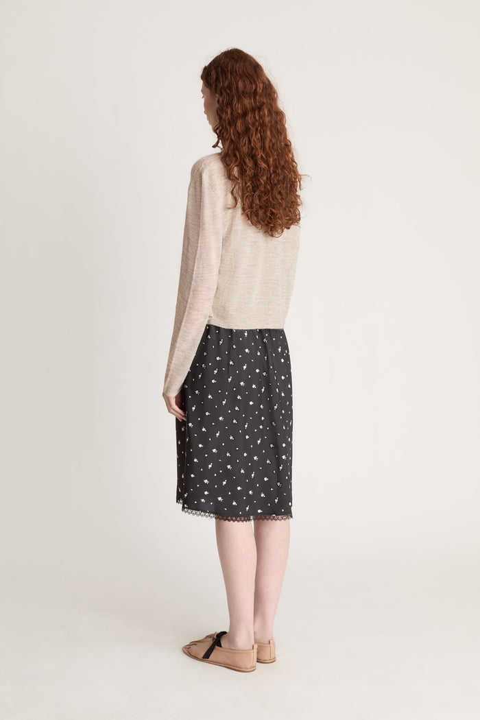 Woman wearing a beige knit cami top and cardigan with a black printed skirt on a white background