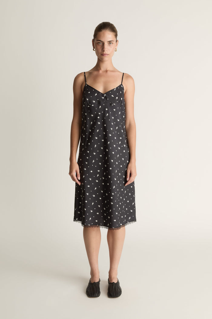 Woman wearing a black slip dress with white floral print on a plain background