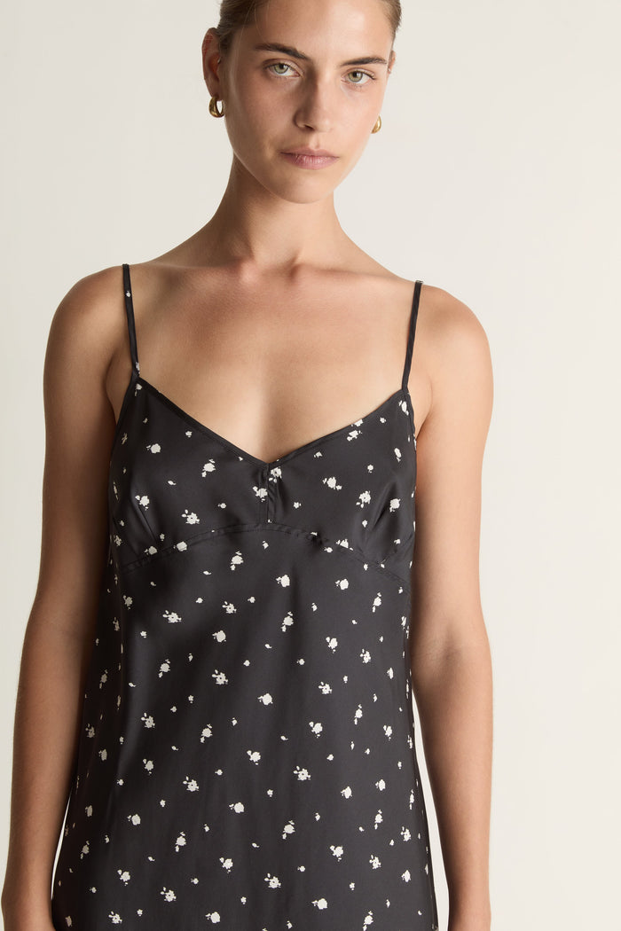 Woman wearing a black slip dress with white floral print on a plain background