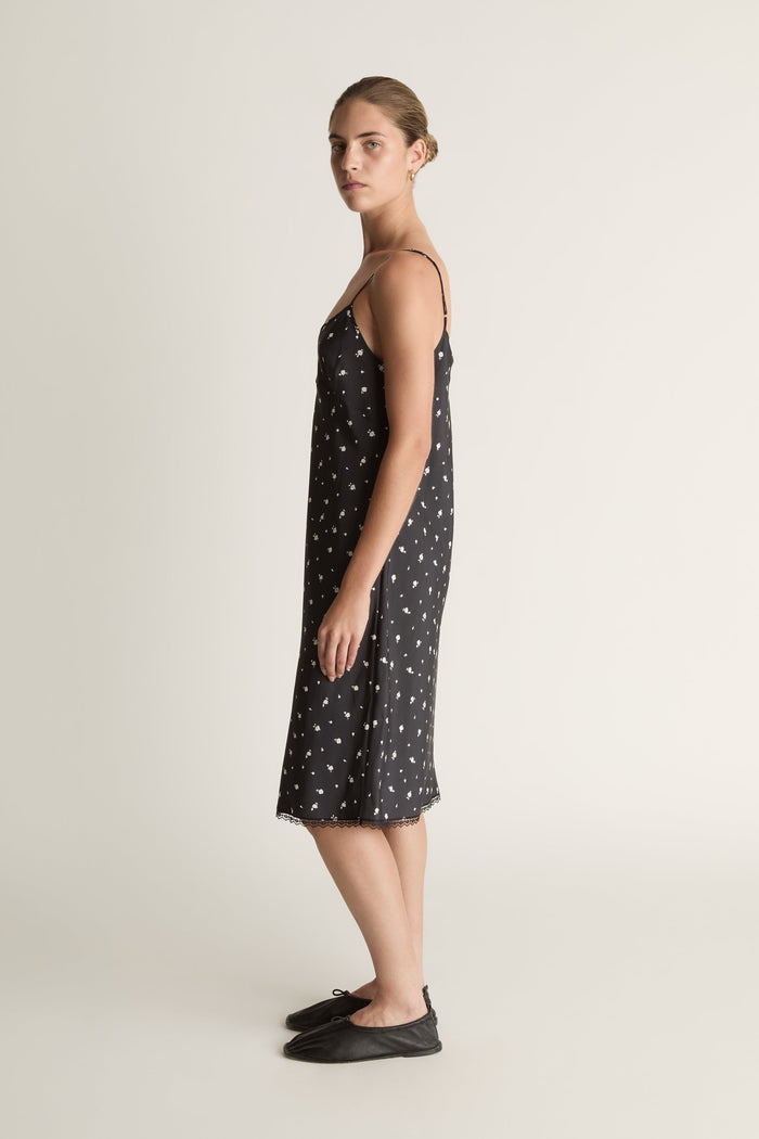 Woman wearing a black slip dress with white floral print on a plain background
