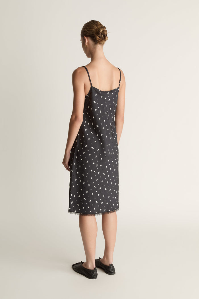 Woman wearing a black slip dress with white floral print on a plain background