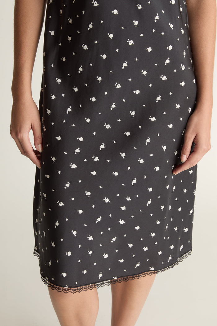 Woman wearing a black slip dress with white floral print on a plain background