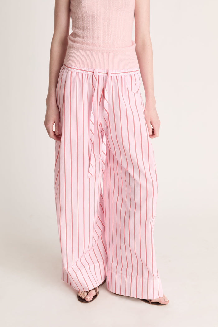 Close up of a woman wearing pink knit top with pink striped pants on a white background